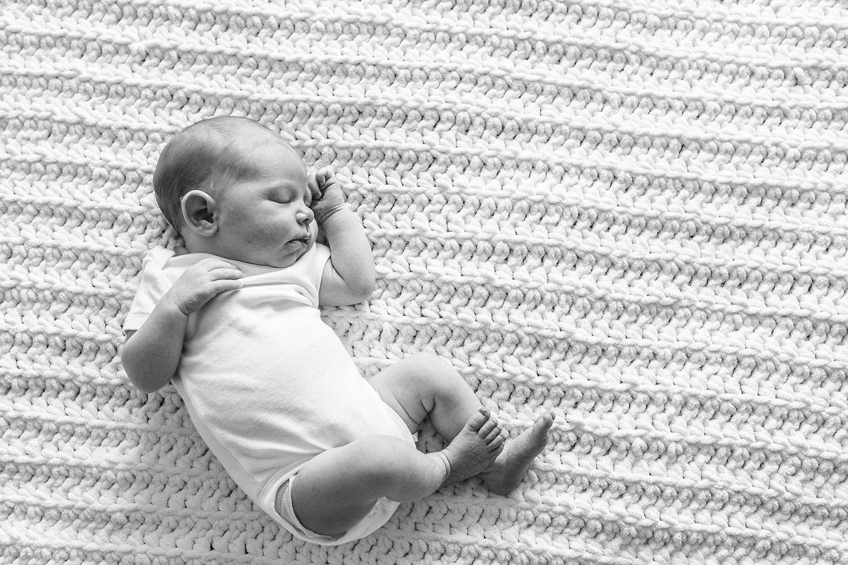 Timeless and natural newborn baby in white onesie sleeping on a textured knit blanket in black and white.