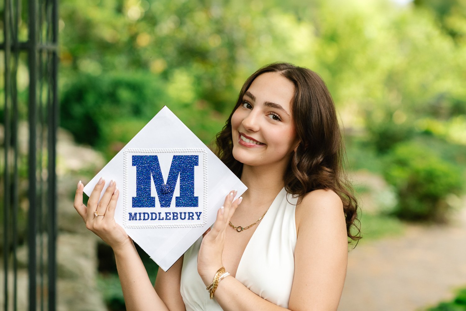 Close up female high school senior with dark hair holding her white graduation cap with studded Middlebury College emblem