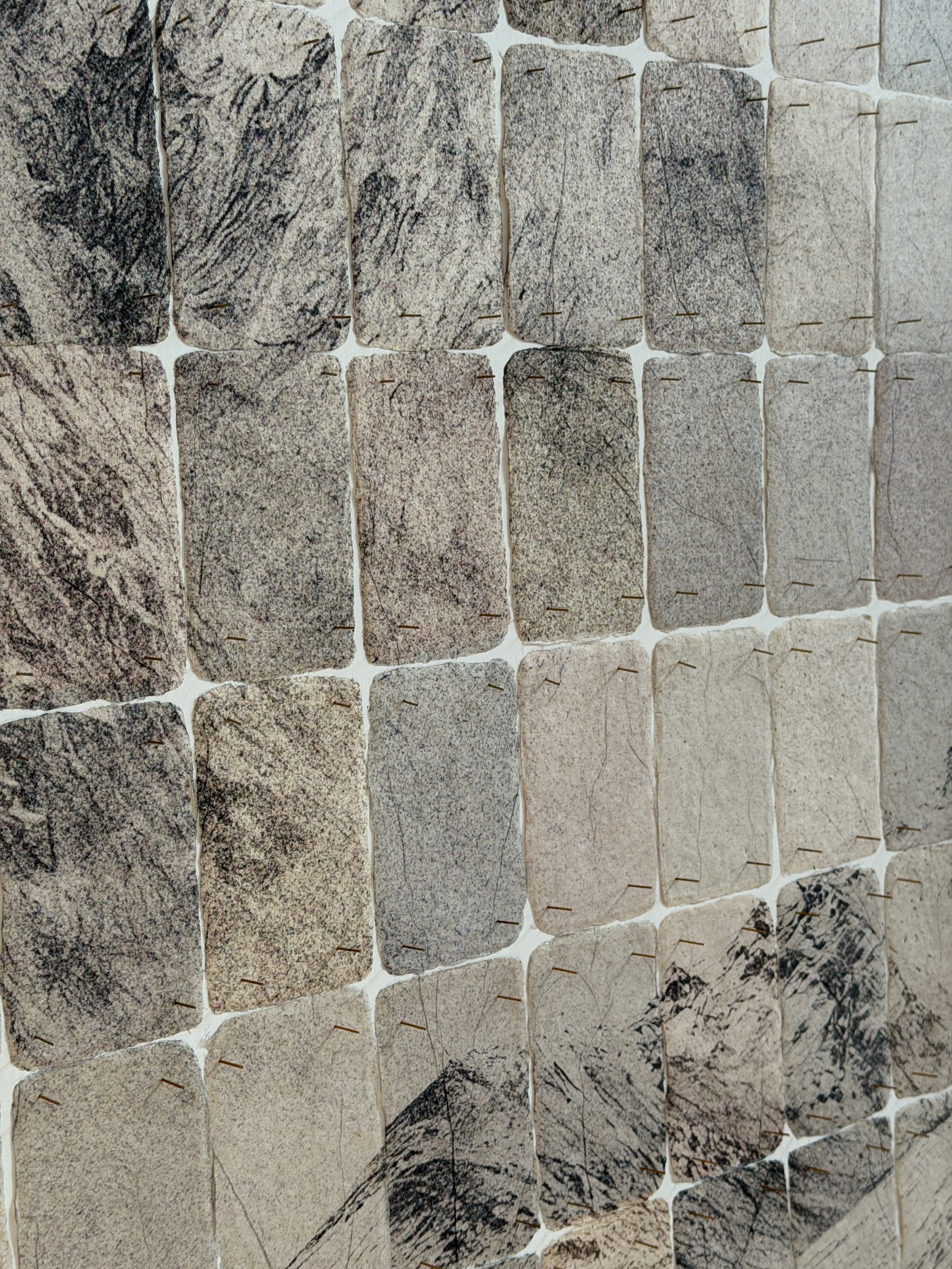 Detail of a mountain landscape assembled from rows of rough-edged photographic cards held with small pins.