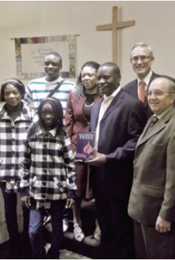   Pastor Roberson Mbayamvula, a church leader from the Democratic Republic of Congo—with wife Caris and children Joel, Divine and Merveille—holds a volume from the set of Believers Church Commentaries provided by Hagerman Mennonite Church, Markham, Ont., during his installation service on Dec. 16, 2012. Also pictured are Earl Smith, chair of the Hagerman discipleship team, front right, and Henry Paetkau, Mennonite Church Eastern Canada area church minister, back right, who led the service.     Photo by Mieke Rumansara  