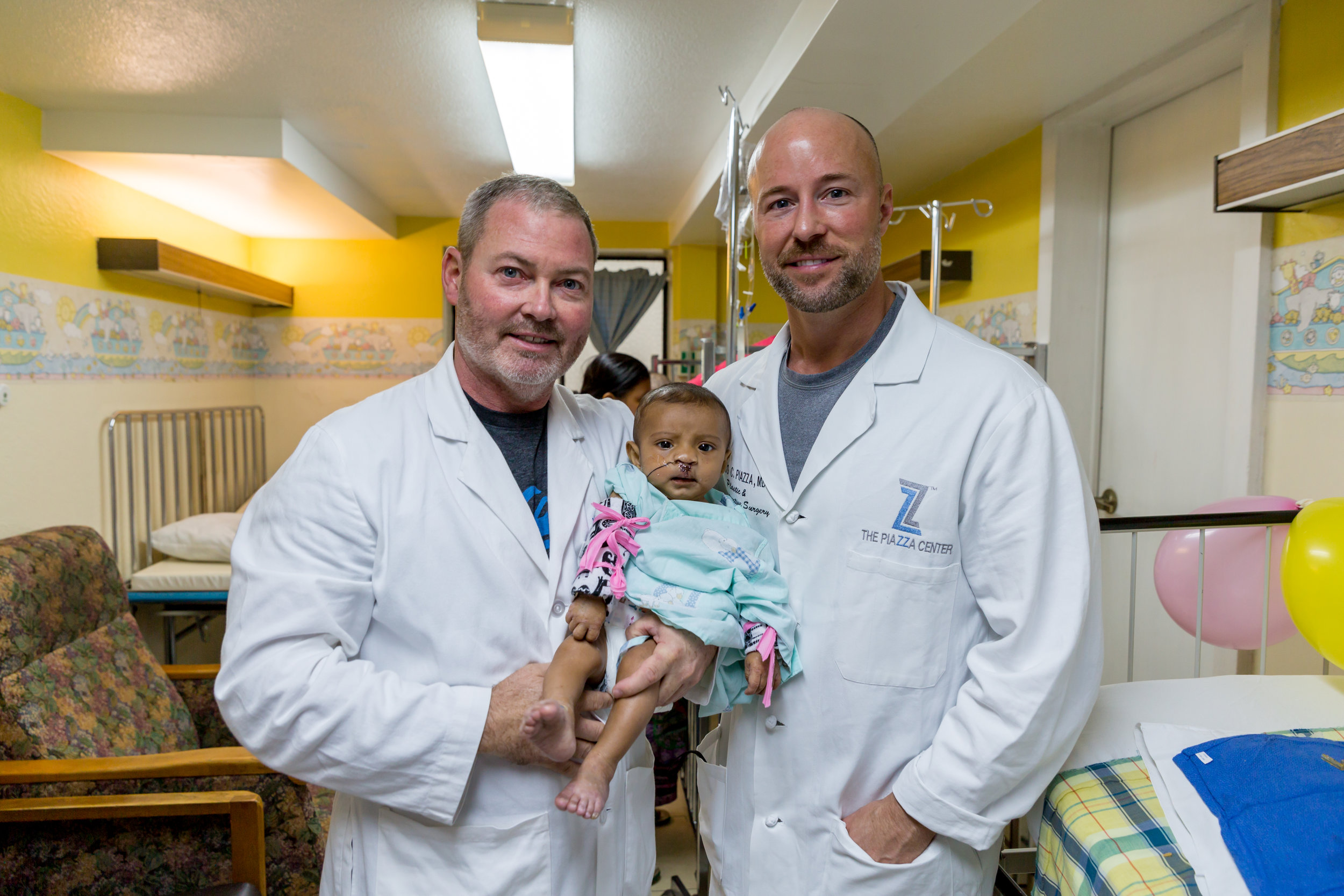 Dr. Patrick Kelley and Dr. Rocco Piazza with Erick post-op after his bilateral cleft lip repair.​.jpg