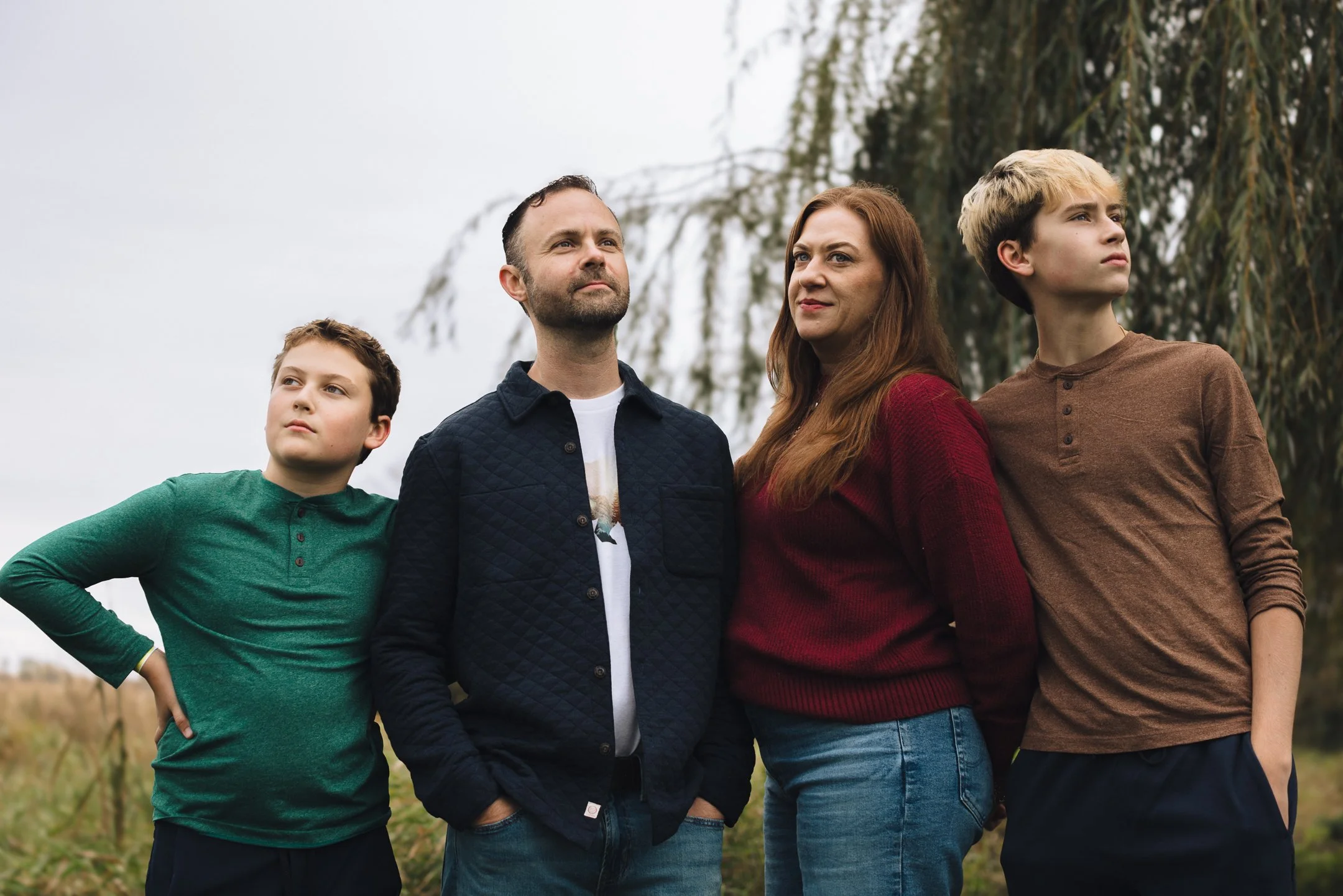 A family of four, standing outdoors on a cloudy day, looking into the distance with serious expressions.