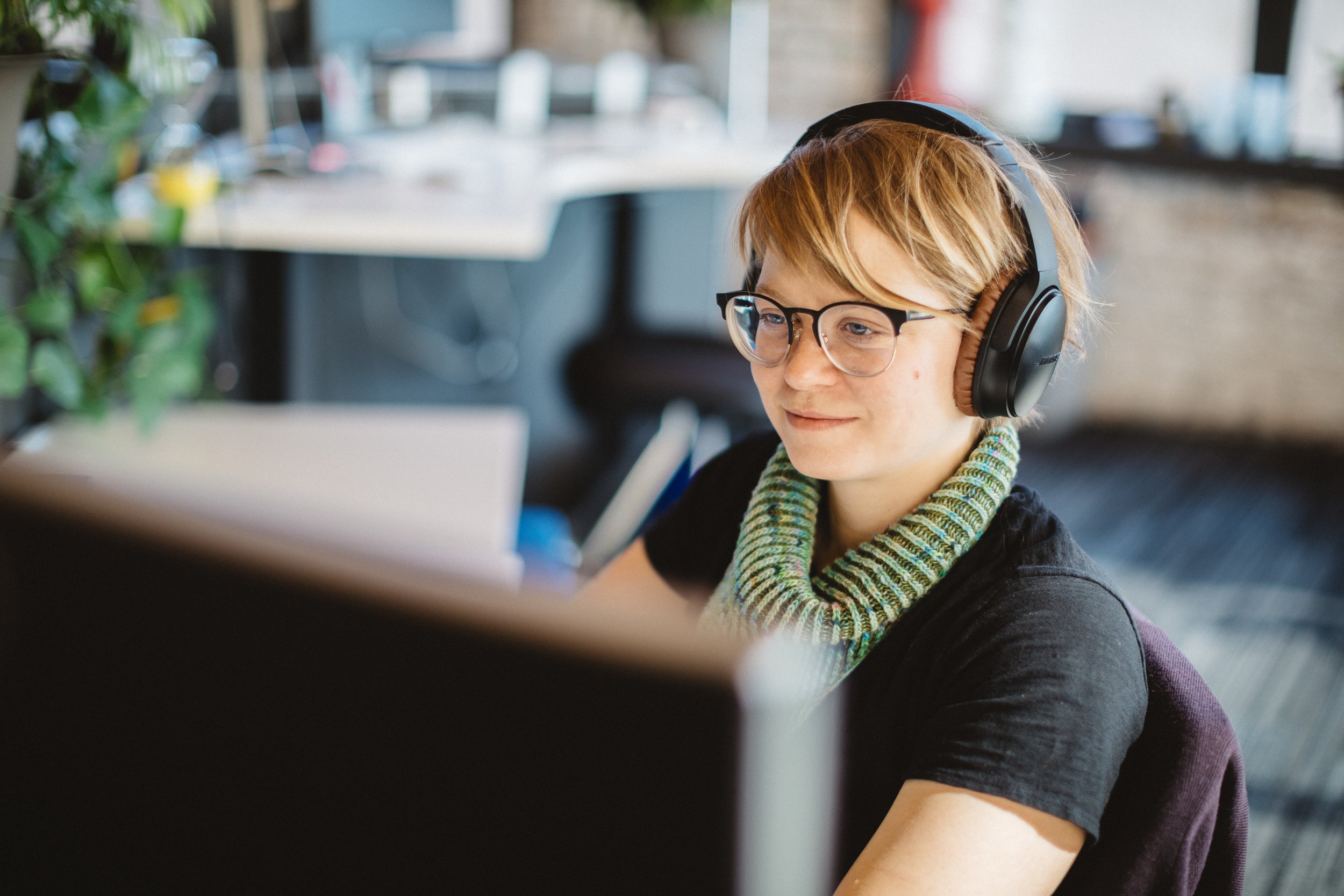 Young woman with short hair, glasses, and headphones working at her desk in a modern office.