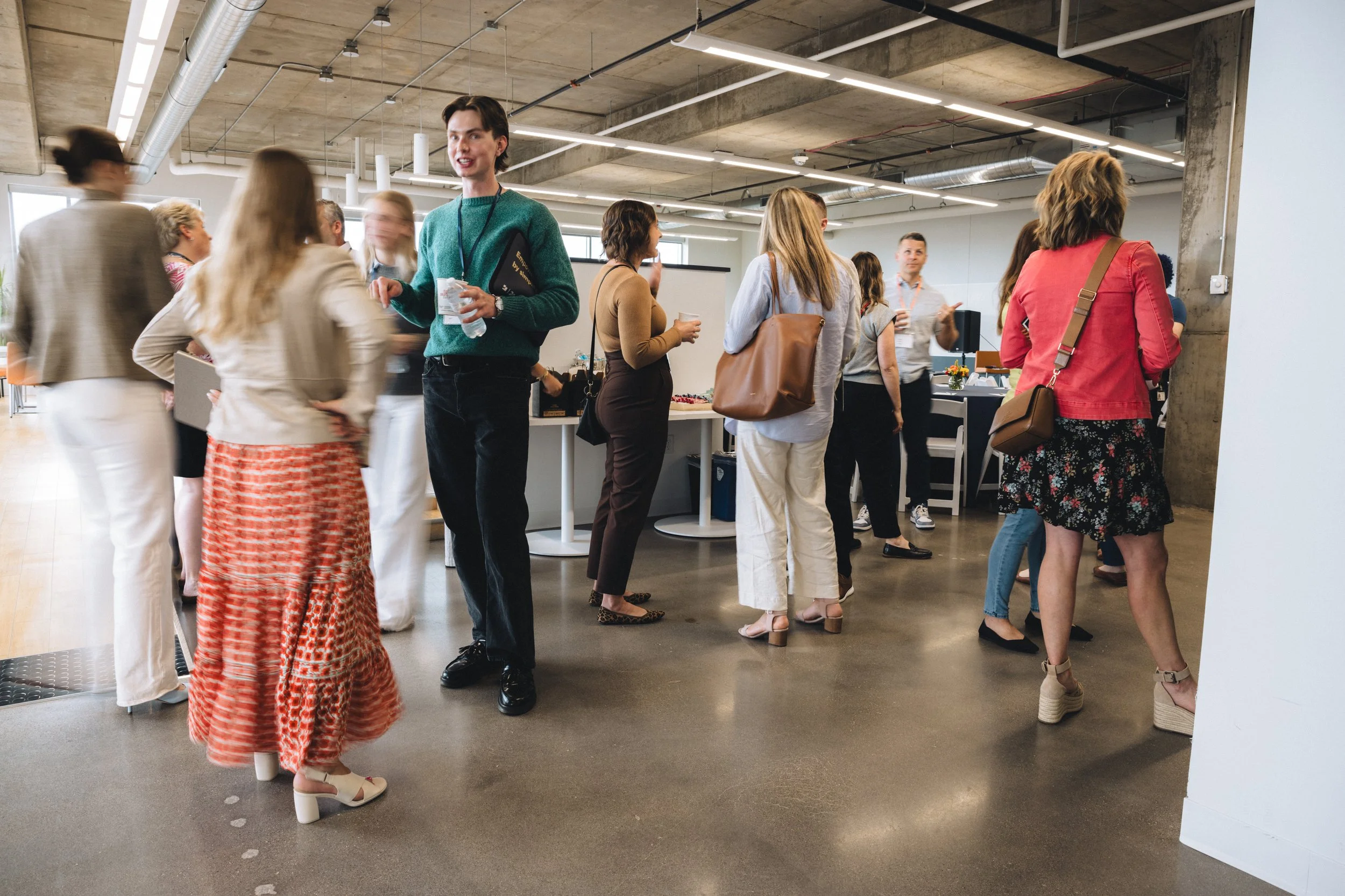 Group of people at a networking event in a modern, industrial-style office space with concrete ceiling and exposed pipes.