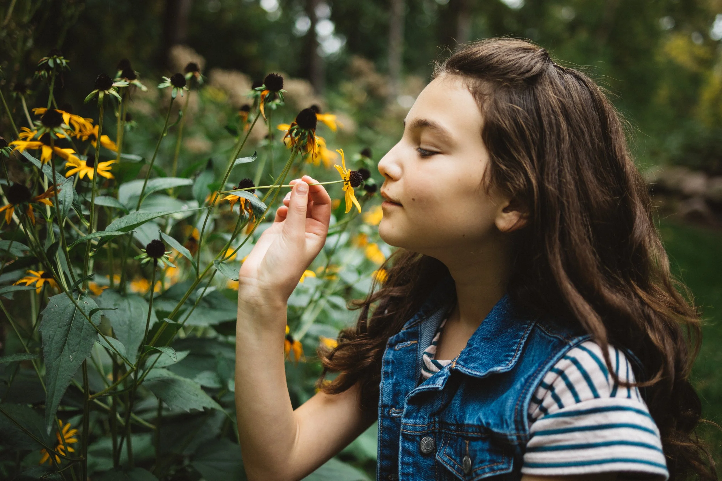 A young girl smelling yellow flowers in a garden