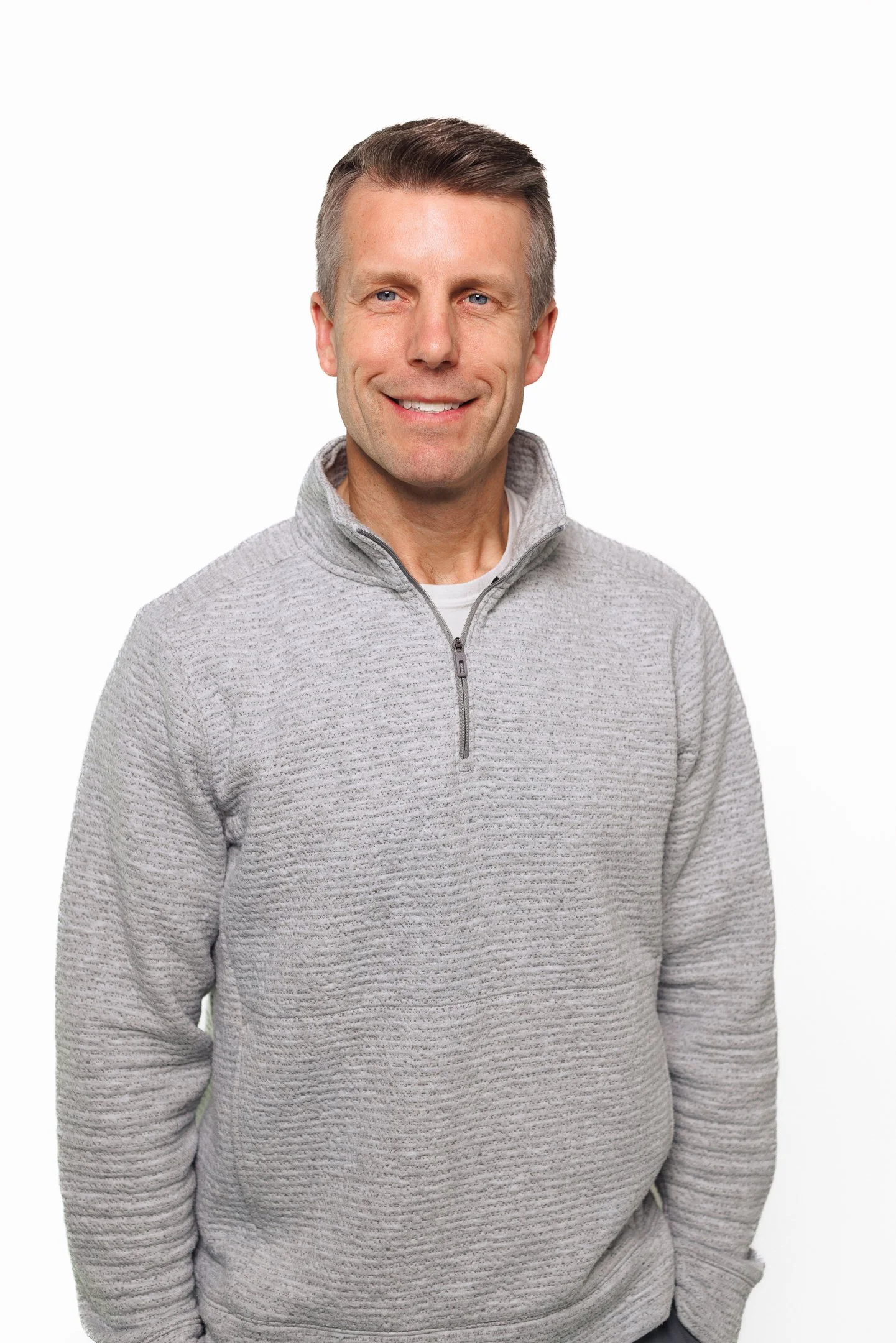 Portrait of a smiling man in a gray quarter-zip sweater against a white background.