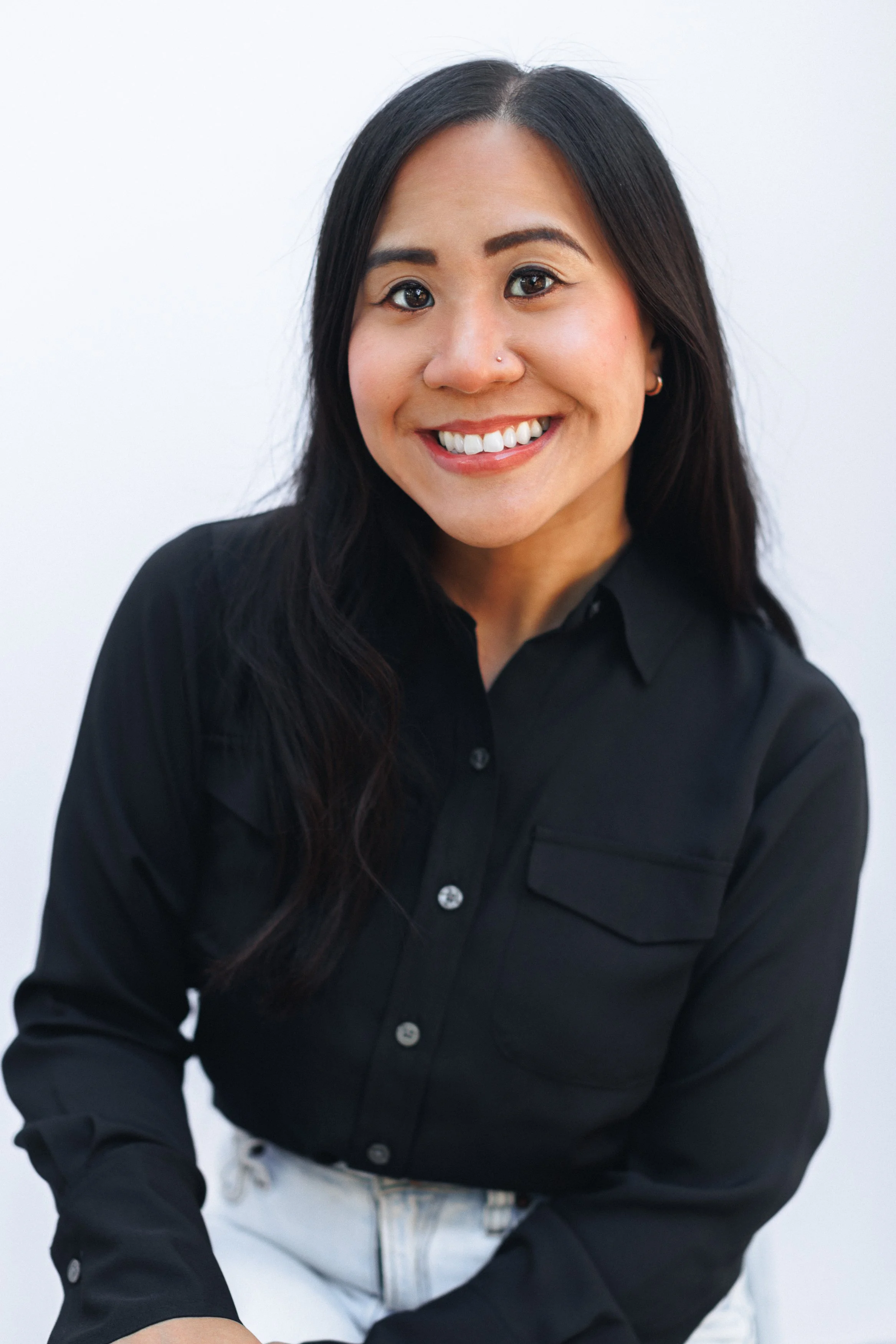 A woman with long black hair, smiling, wearing a black shirt, against a white background.