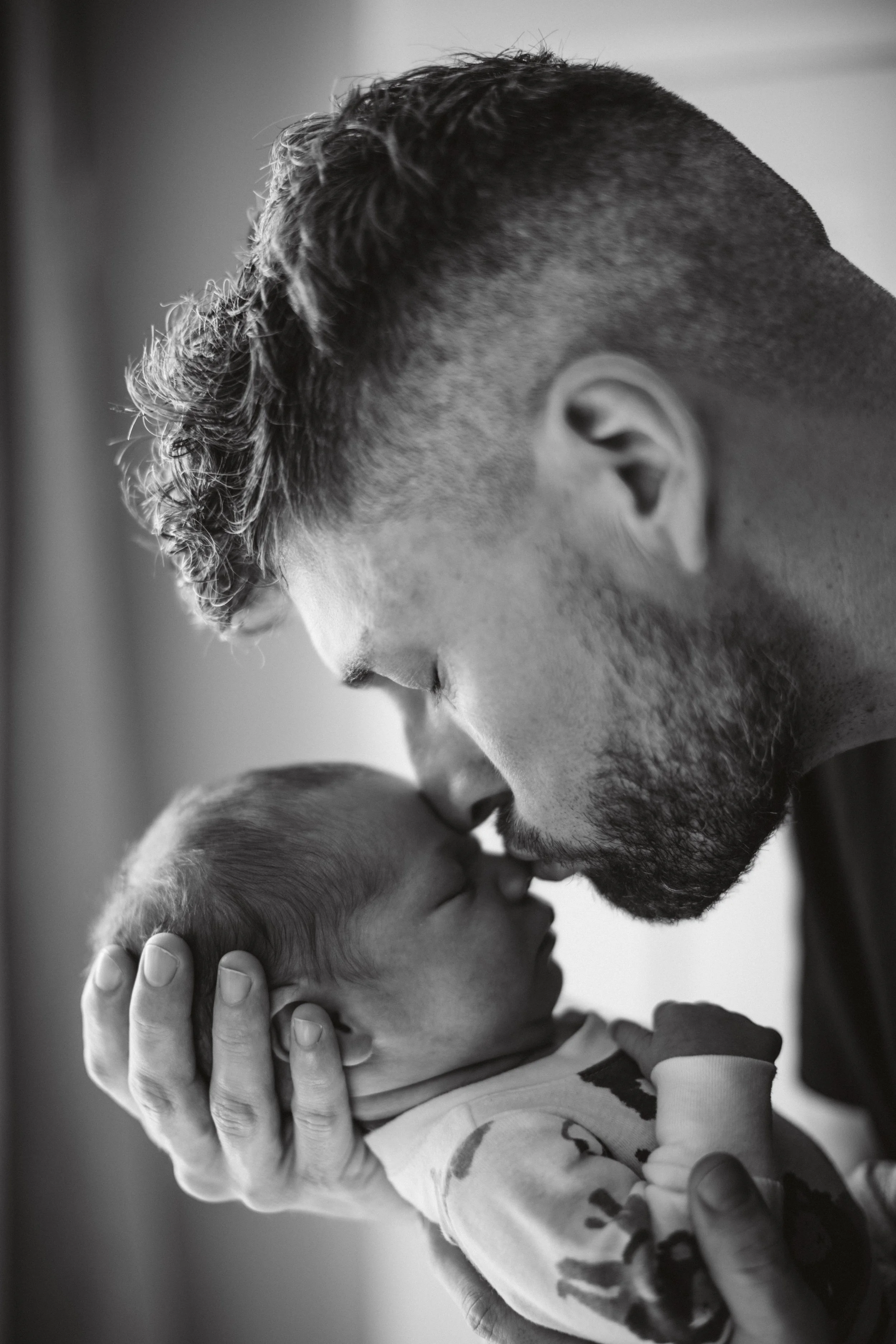 A black and white photo of a man holding a newborn baby close, with their foreheads touching in a tender moment.