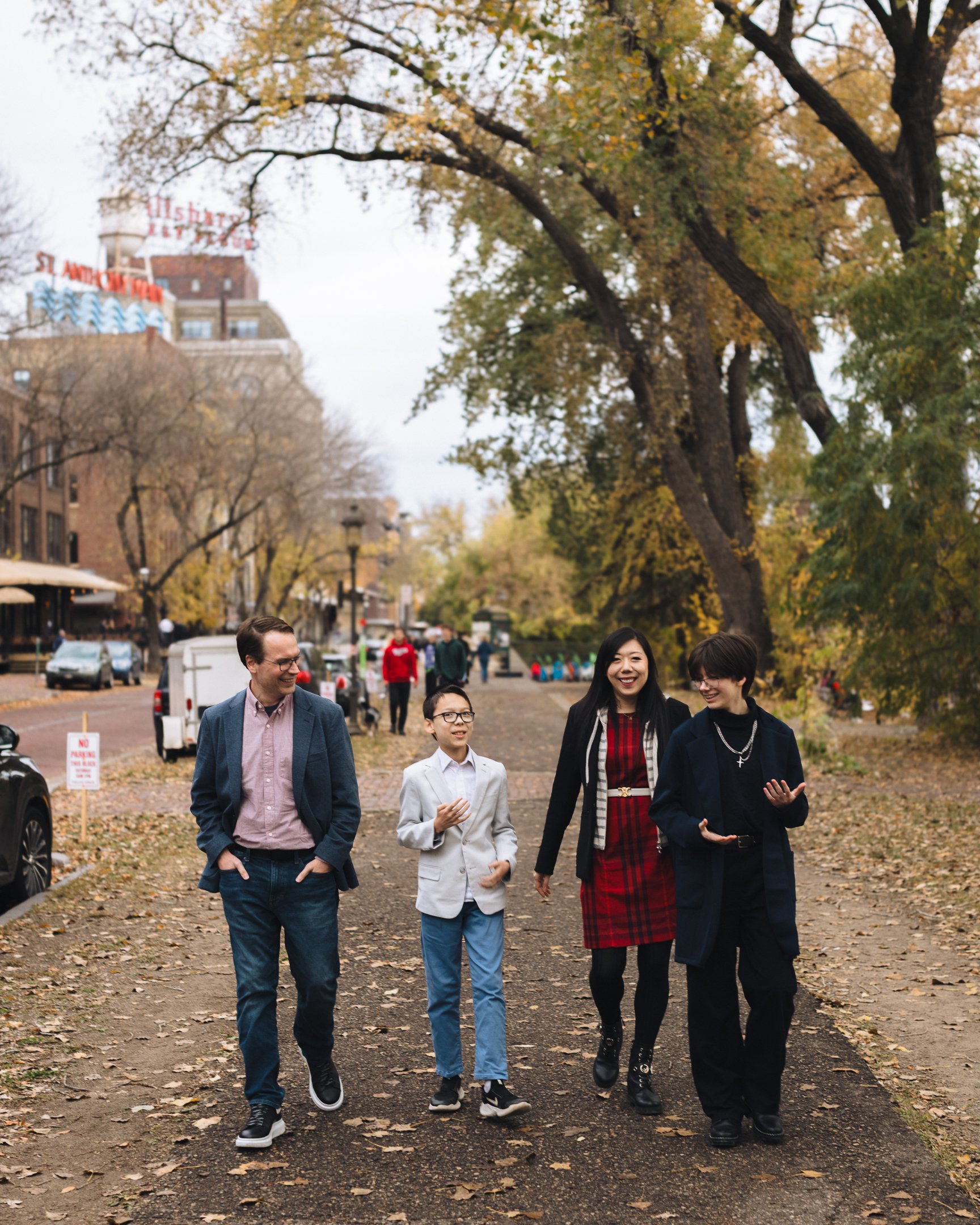 Group of four people walking and talking in a park during autumn, with trees and buildings in the background.