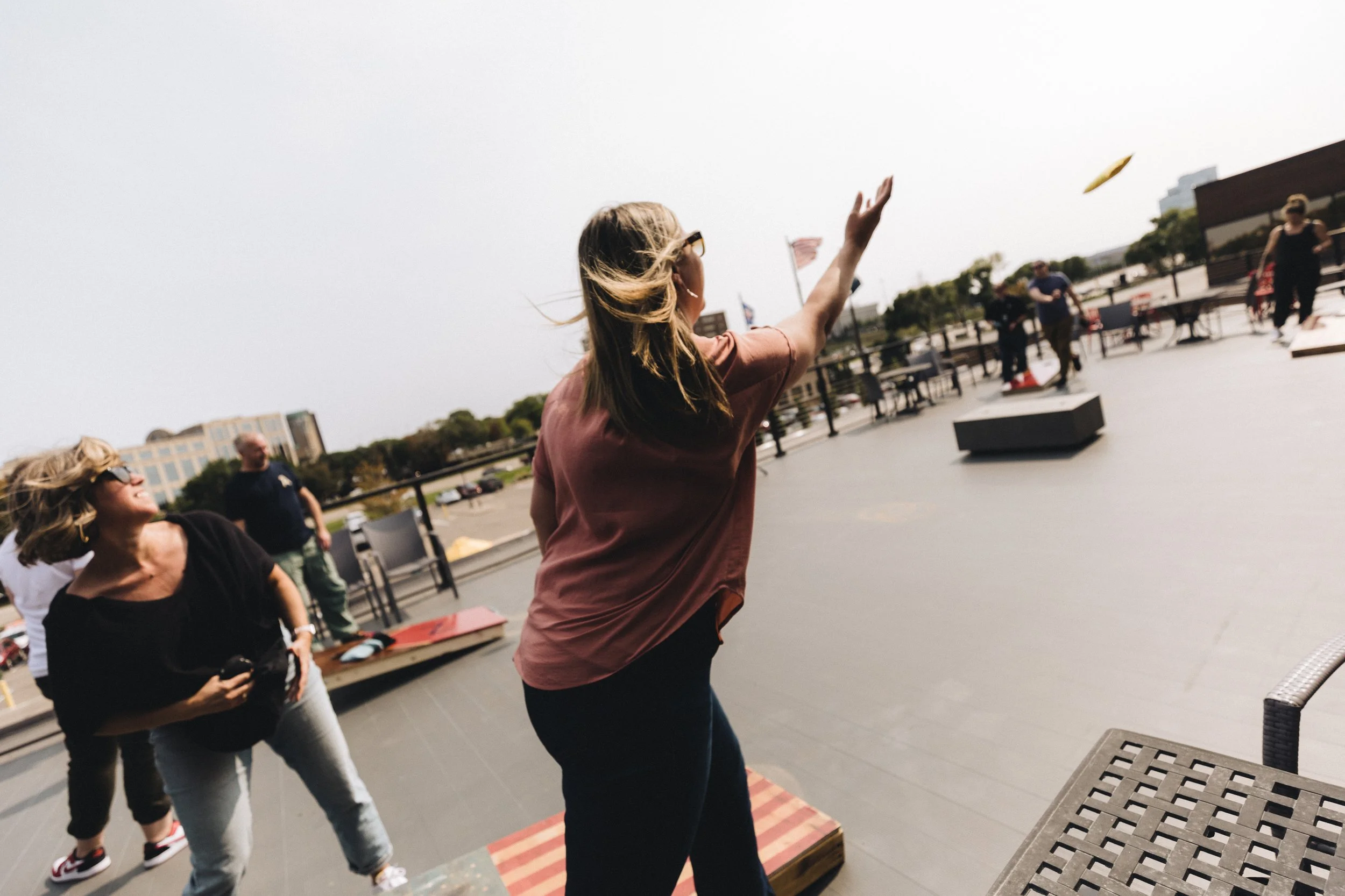 Women playing cornhole outdoors on a sunny day with a cloudy sky.