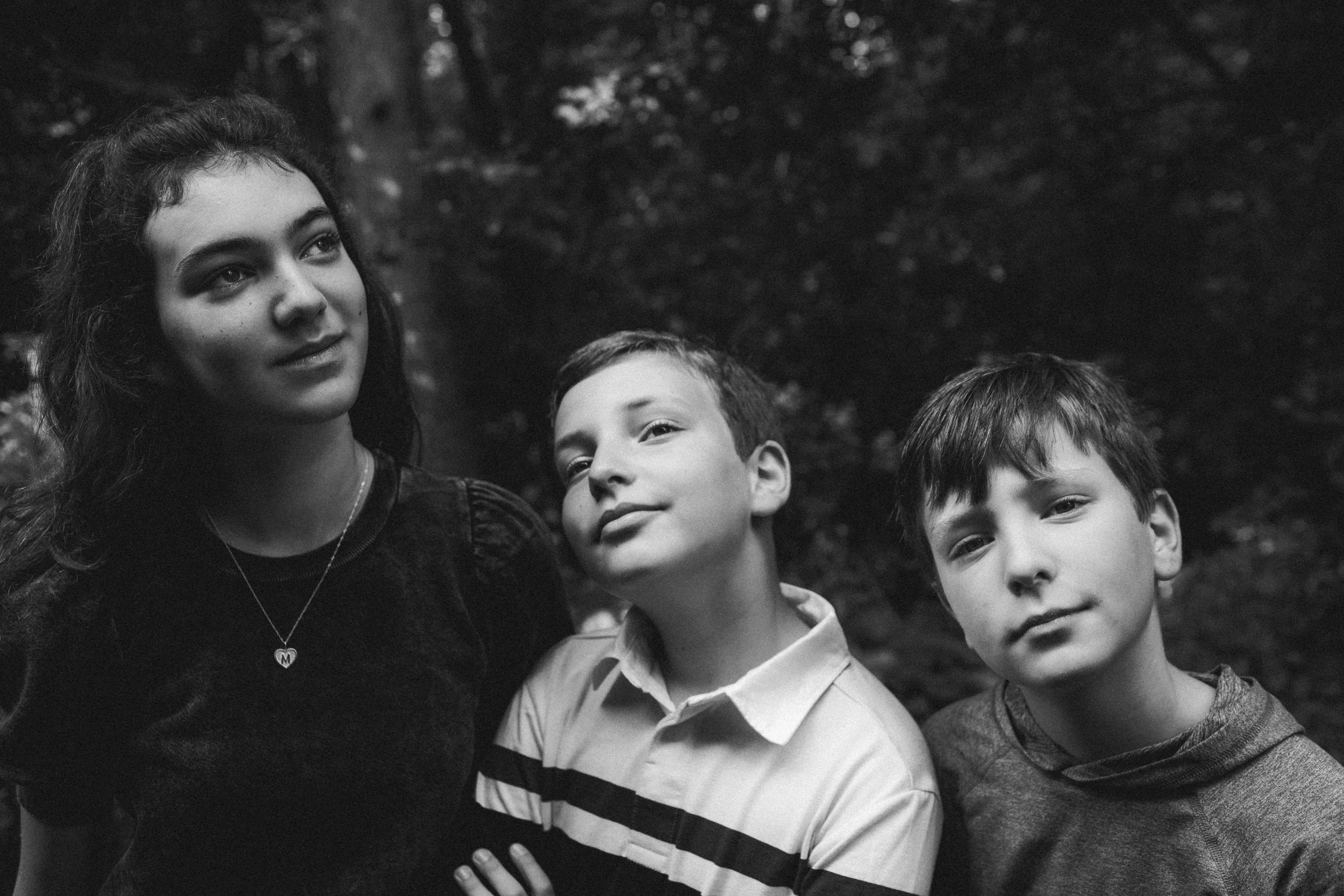 Black and white photo of three children outdoors, two boys and a girl, standing close together, looking confident and relaxed.