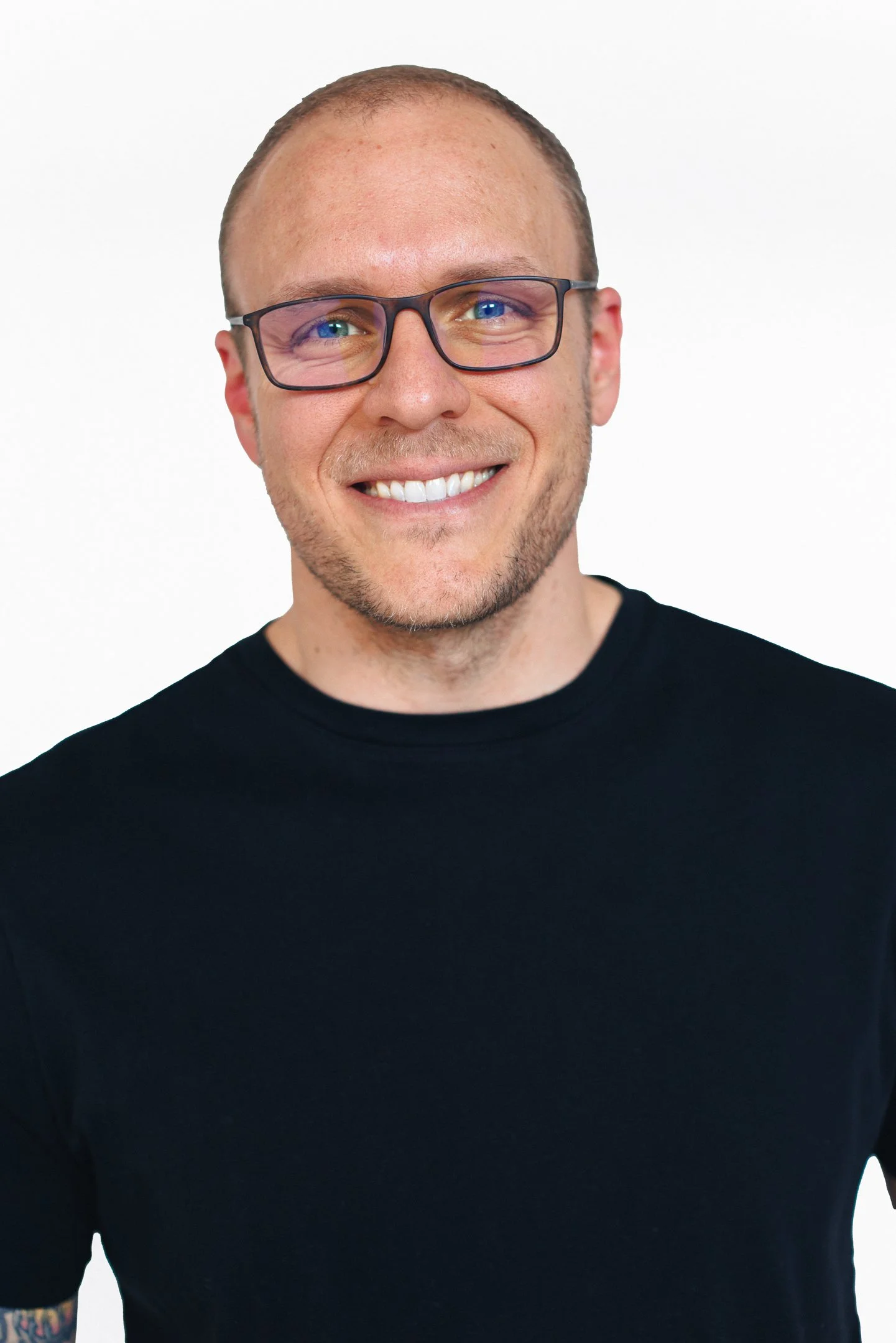 A man with glasses, a beard, and short hair smiling in front of a white background.