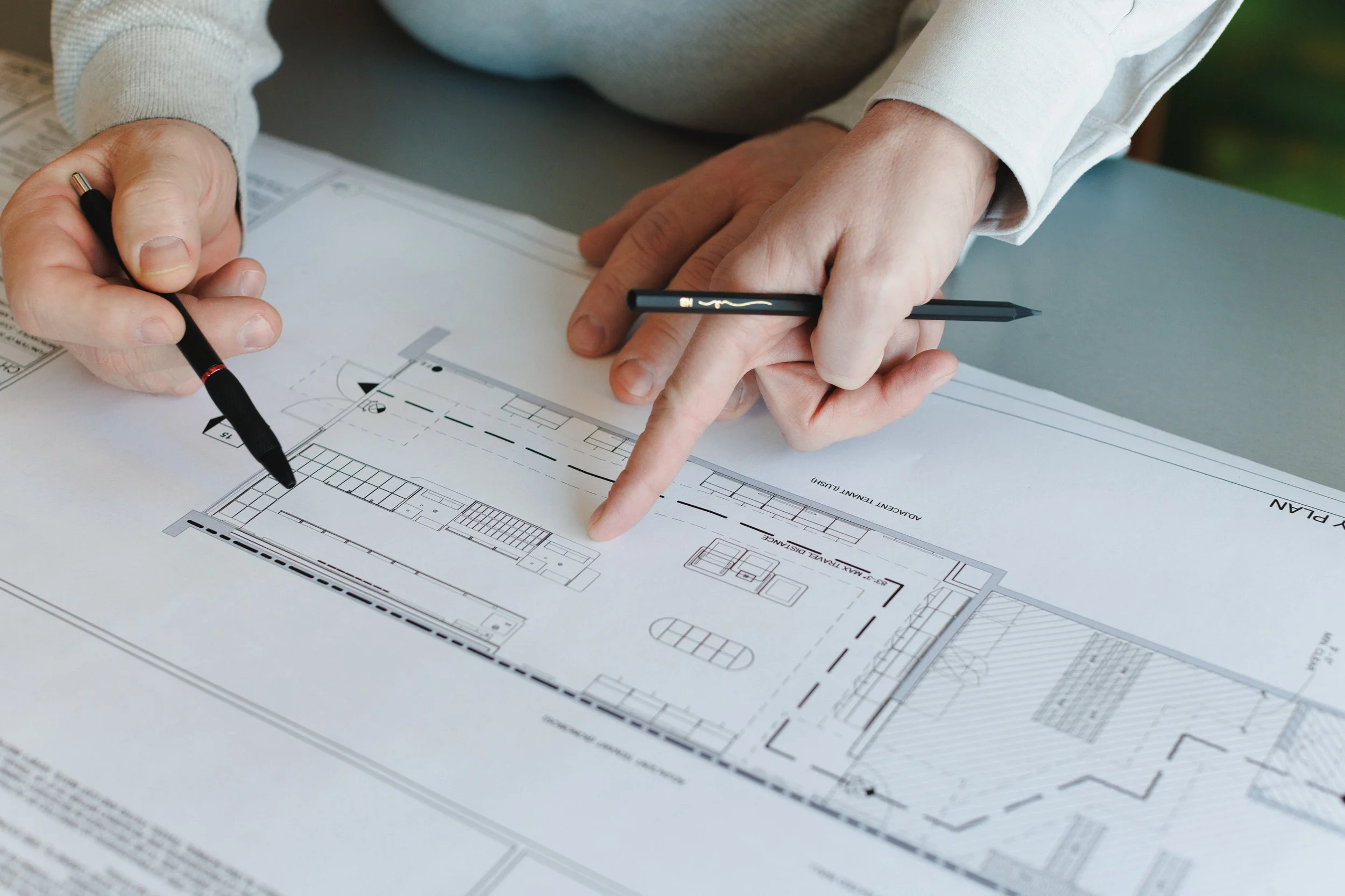 Person reviewing architectural blueprints, pointing and holding pencils.