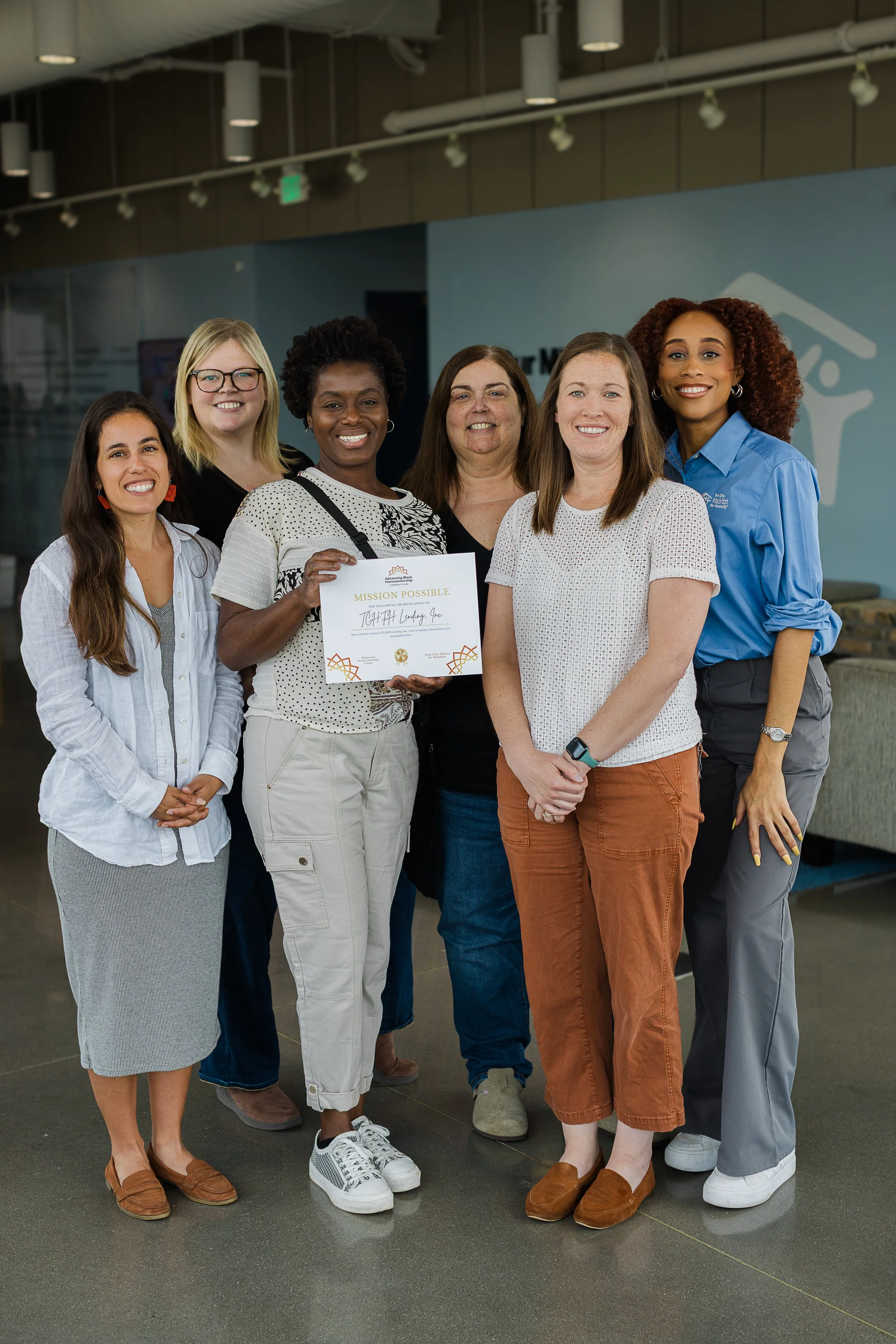Group of six women standing together indoors, smiling, with one holding a certificate labeled 'Mission Possible'.