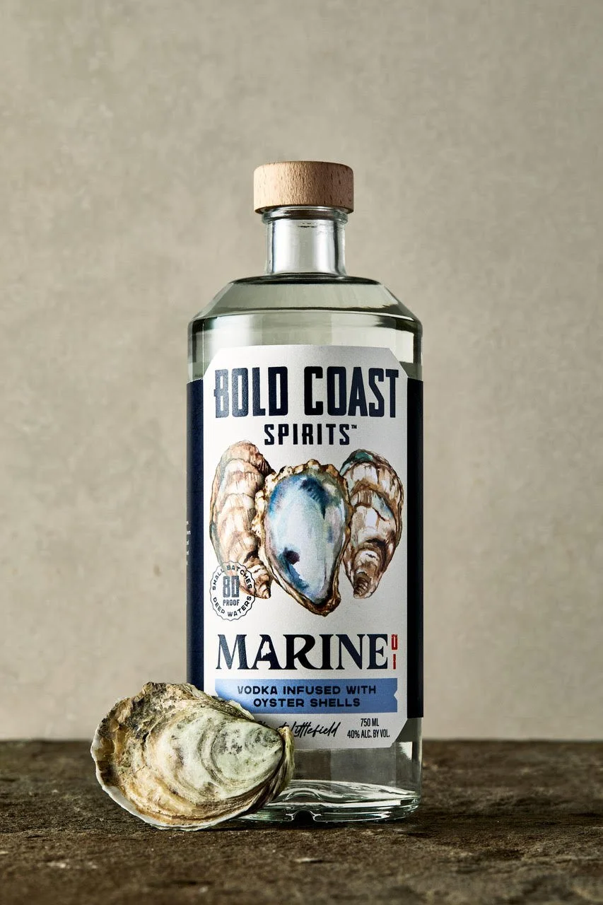 Close-up of Bold Coast Spirits bottle packaging featuring hand-painted oyster shell watercolor artwork with iridescent blue and grey tones