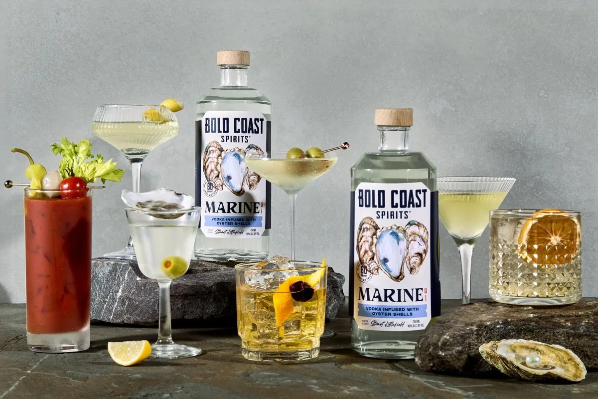 Bold Coast Spirits bottles and cocktails styled together, showcasing coastal-inspired packaging with custom oyster shell watercolor illustrations