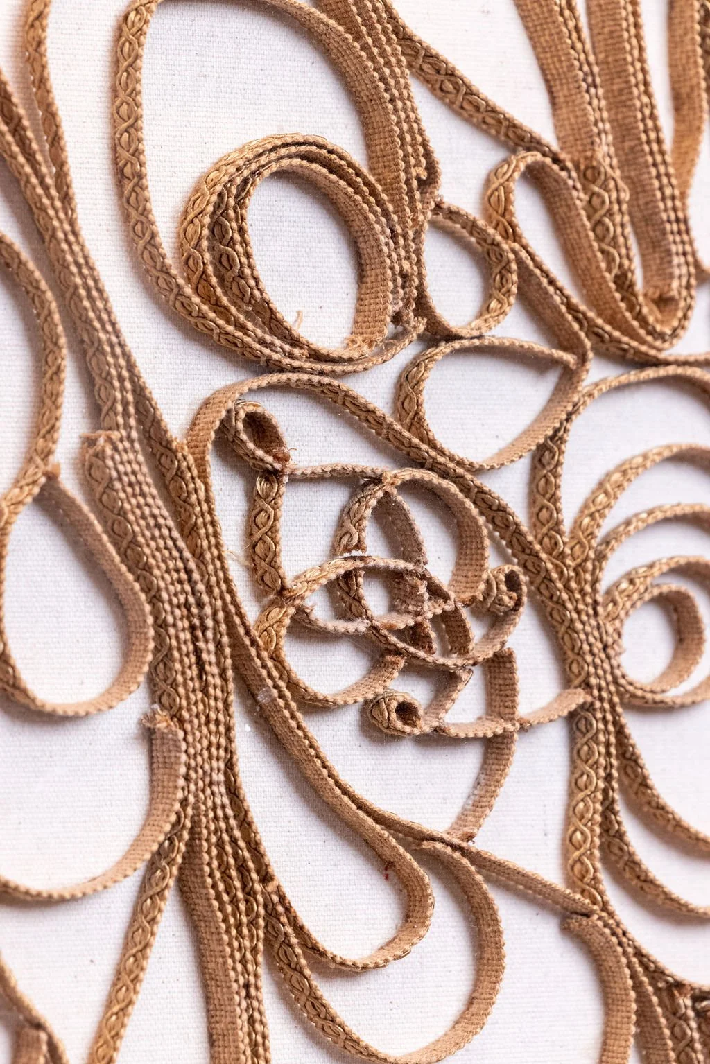 A close-up of tangled, light brown decorative ribbons or trim with intricate patterns on a white background.