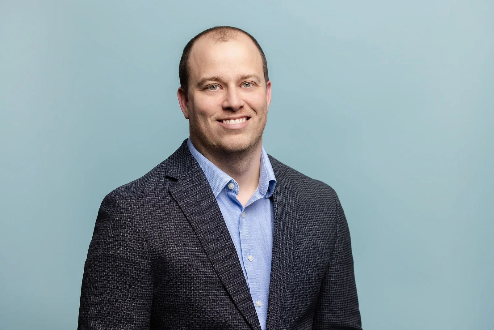 Fluor summit headshot of a man in a dark jacket and light blue shirt against a blue background