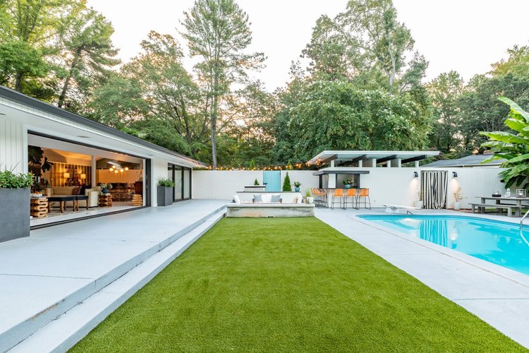 Modern backyard with pool, outdoor seating, bar area, and sliding glass door leading inside a house.