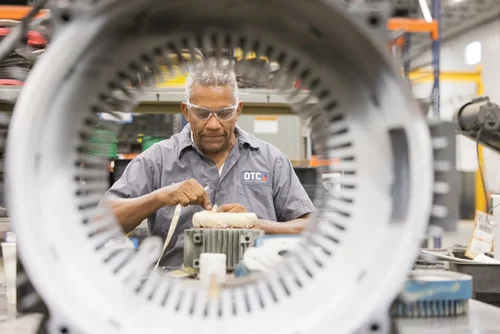 Technician framed through an electric-motor stator at OTC Industrial Technologies, a still from the OTC facility film by Jack Robert Photo