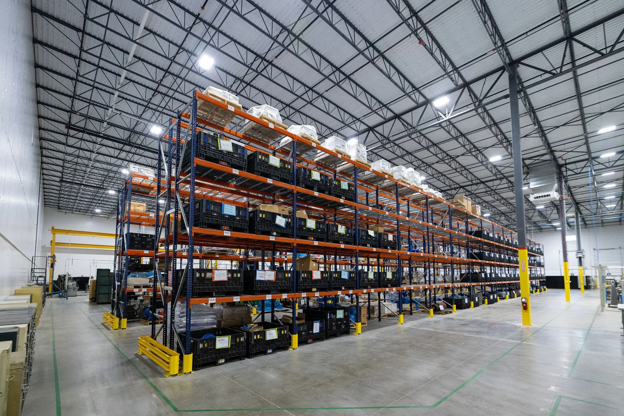 Interior view of a warehouse with high ceiling and metal shelves stocked with boxes and plastic containers.