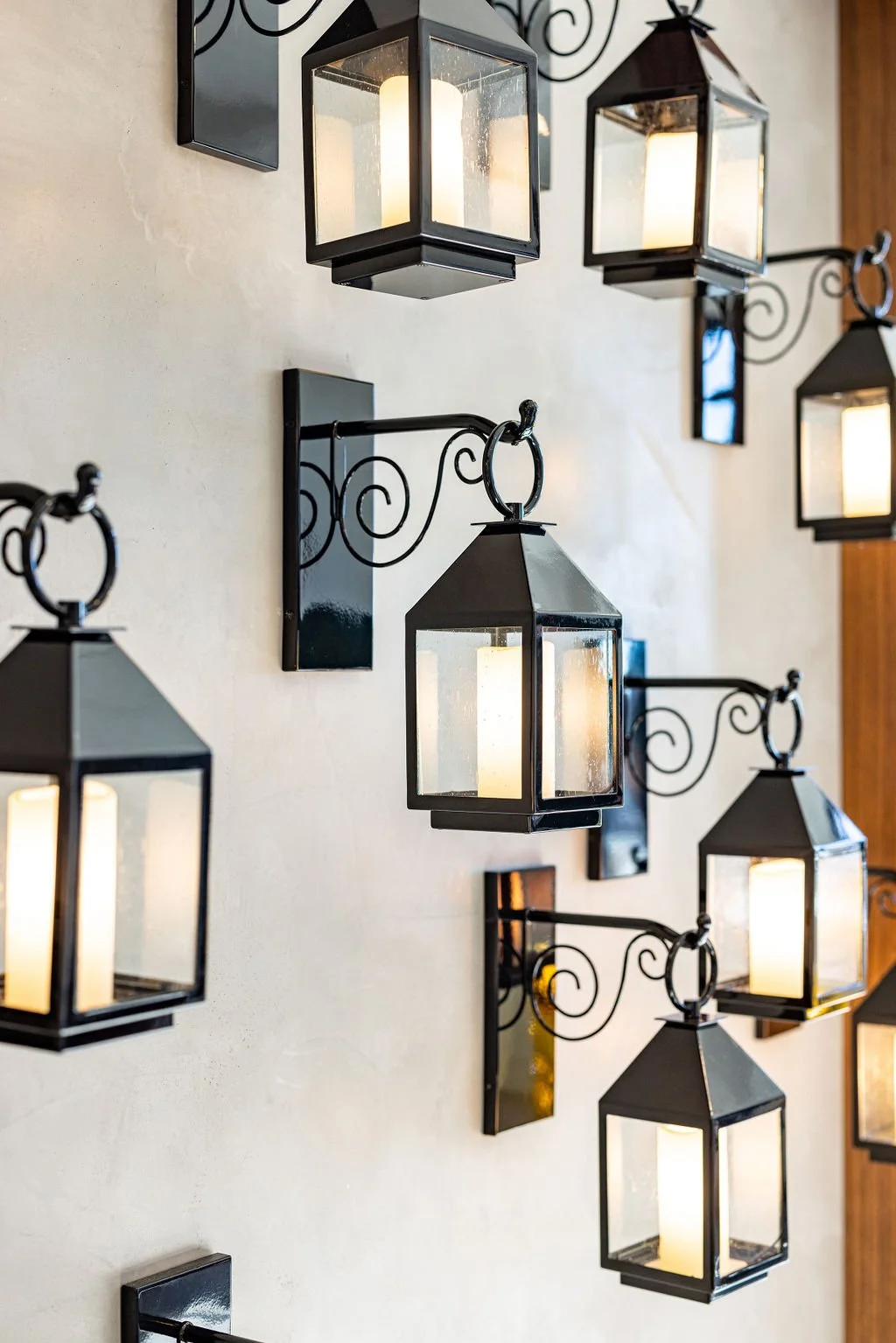Multiple black-framed lantern-style wall sconces with white candles inside, mounted on a light-colored wall.