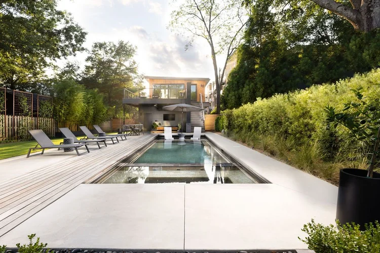Modern backyard with swimming pool, lounge chairs, wooden deck, and lush green landscaping.