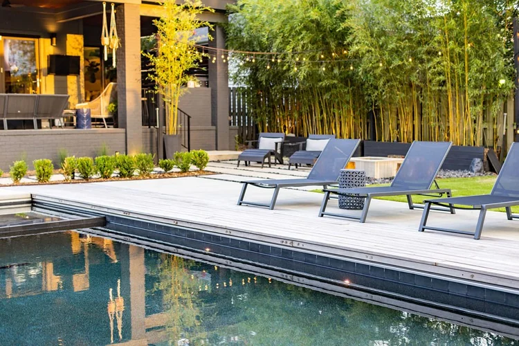 Backyard with pool, lounge chairs, and outdoor seating area surrounded by greenery and string lights.