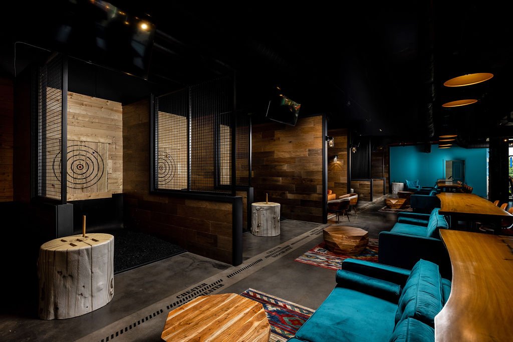 Interior of a modern, stylish bar or lounge with wooden accents, teal and orange seating, and target graphics on the walls.