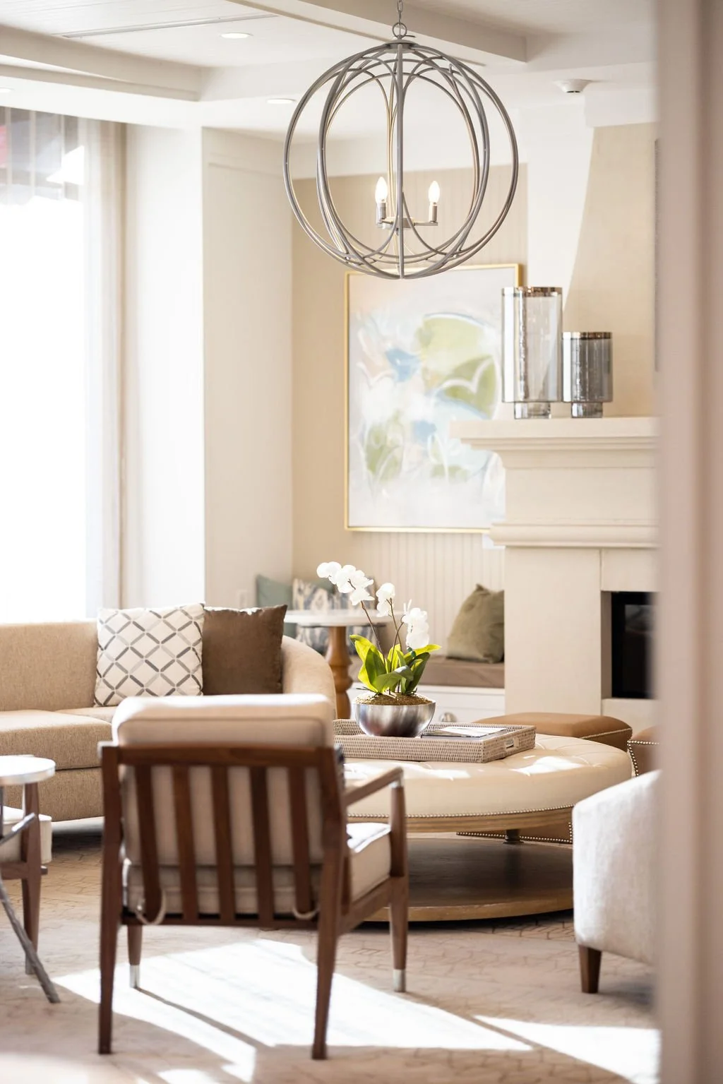 Living room with beige sofa, armchair, coffee table with white orchid plant, abstract wall art, and modern chandelier.