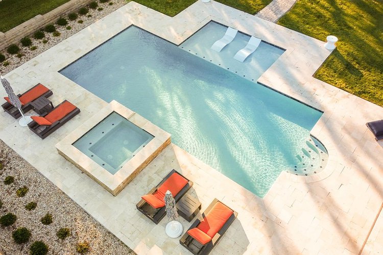 An aerial view of a backyard swimming pool with a hot tub and lounge chairs with umbrellas.