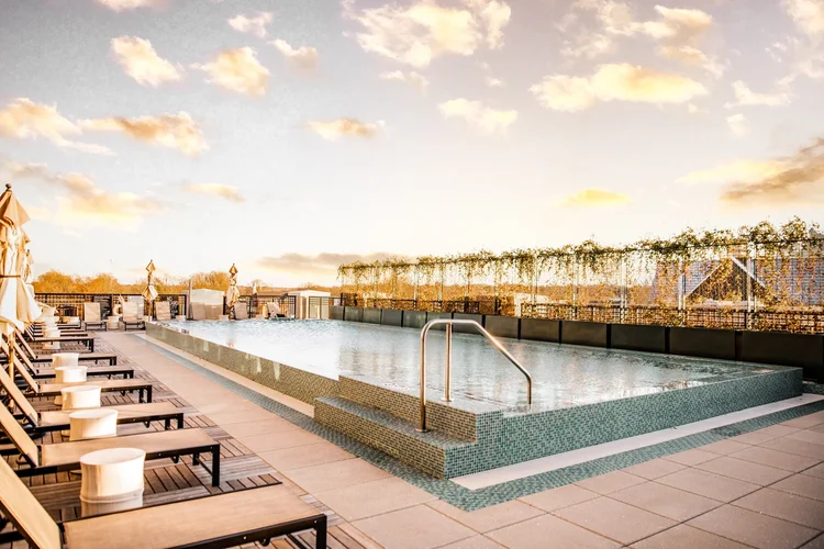 Empty rooftop swimming pool with lounge chairs and umbrellas at sunset.