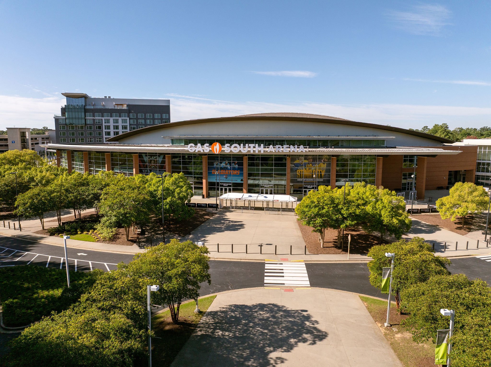 Exterior view of GAS South Arena with trees in the foreground and a parking lot in front. The arena has large glass windows and a sign displaying its name.