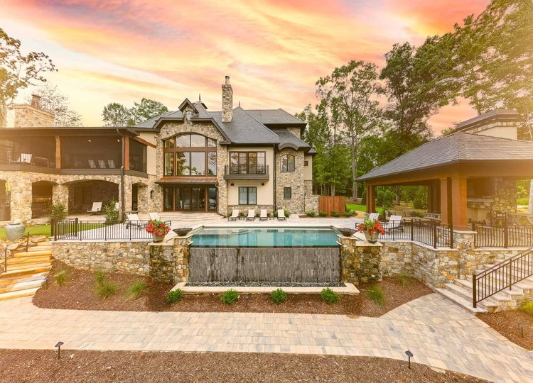 Luxury stone and stucco mansion with an outdoor pool at sunset.
