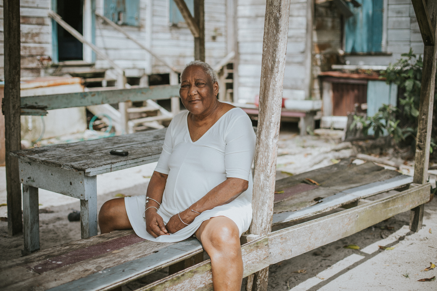  From the shade of her front yard in Gales Point, Belize, retired principal Alicia Parks watches Marymount University students learn how cashew seeds are roasted. Alicia suffers from chronic knee pain and describes her husband as "sick with stroke." 
