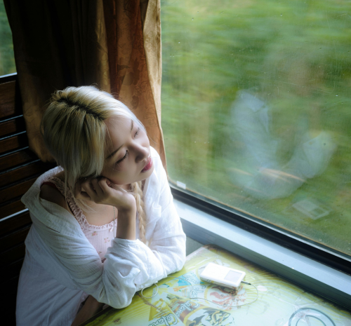 Teenager sitting by window during winter months looking contemplative, representing seasonal emotional struggles