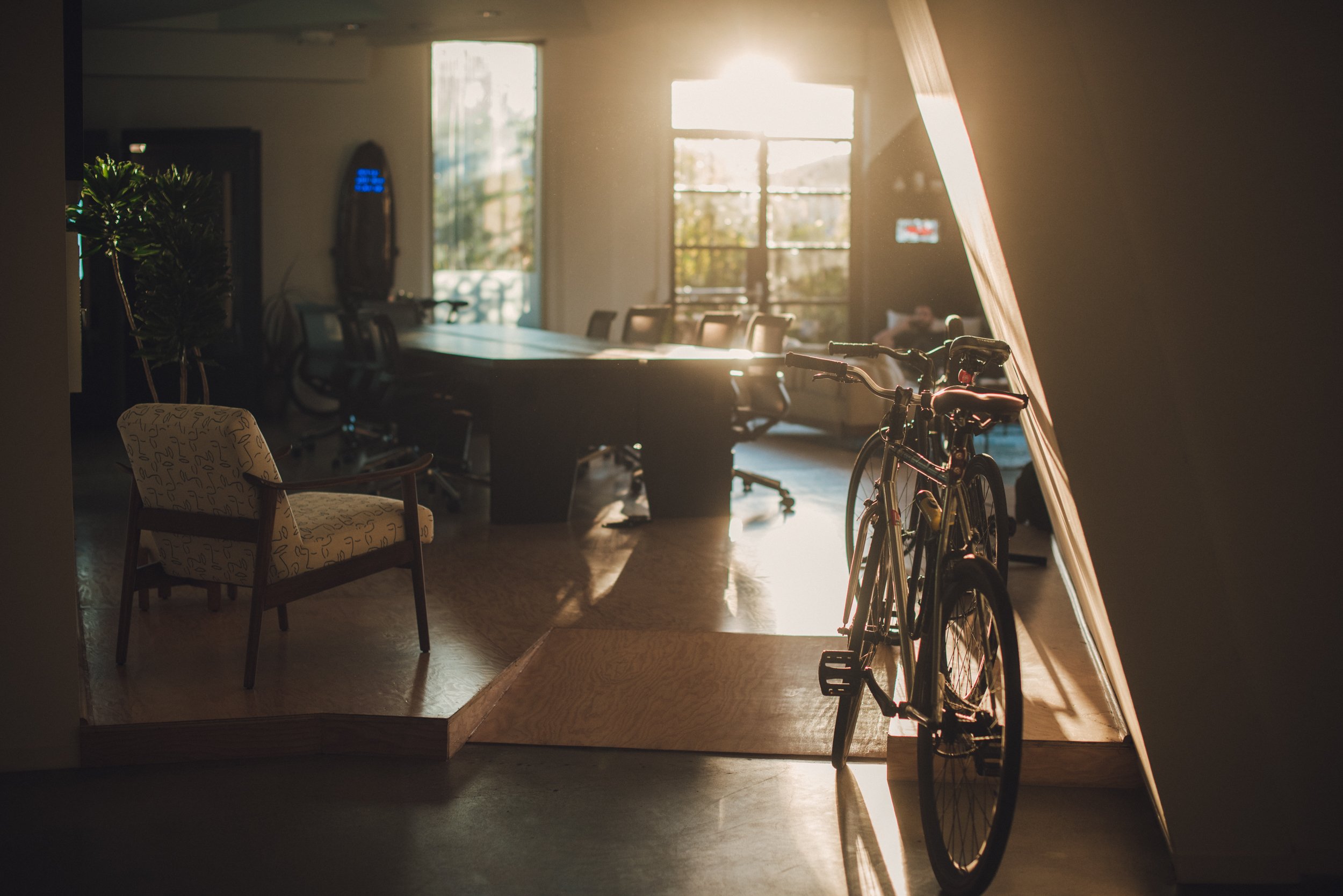 Interior of an office with a bicycle, wooden table, chairs, and sunlight streaming through windows. Media.Monks los Angeles - commercial interior photography