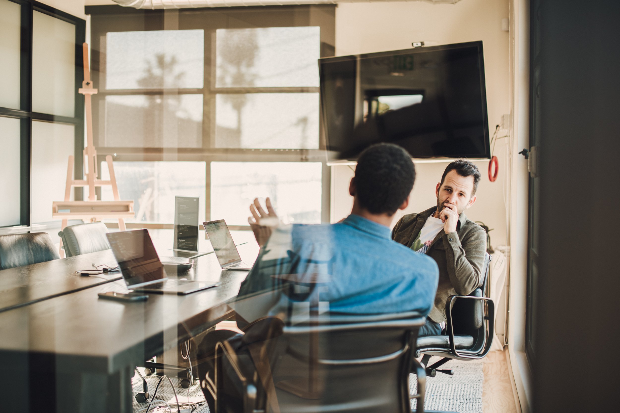 Two men having a discussion in a modern office with laptops and a large monitor. Media.Monks los Angeles - commercial interior photography