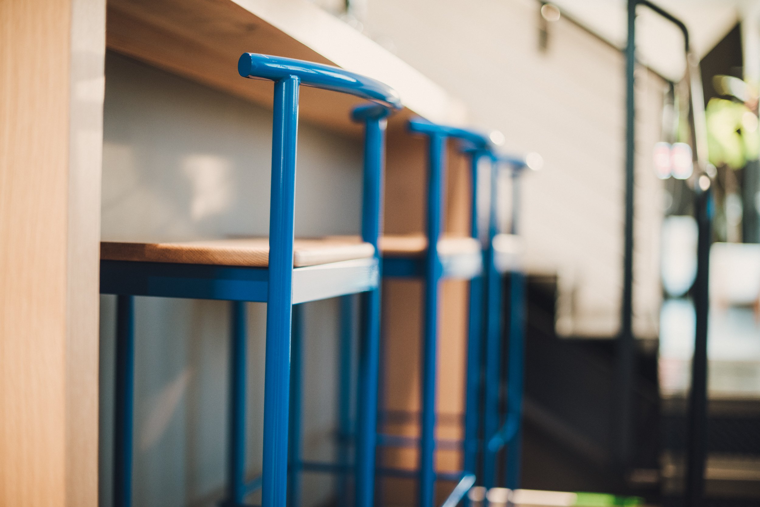 Close-up of blue barstools with wooden seats at a counter. Media.Monks los Angeles - commercial interior photography