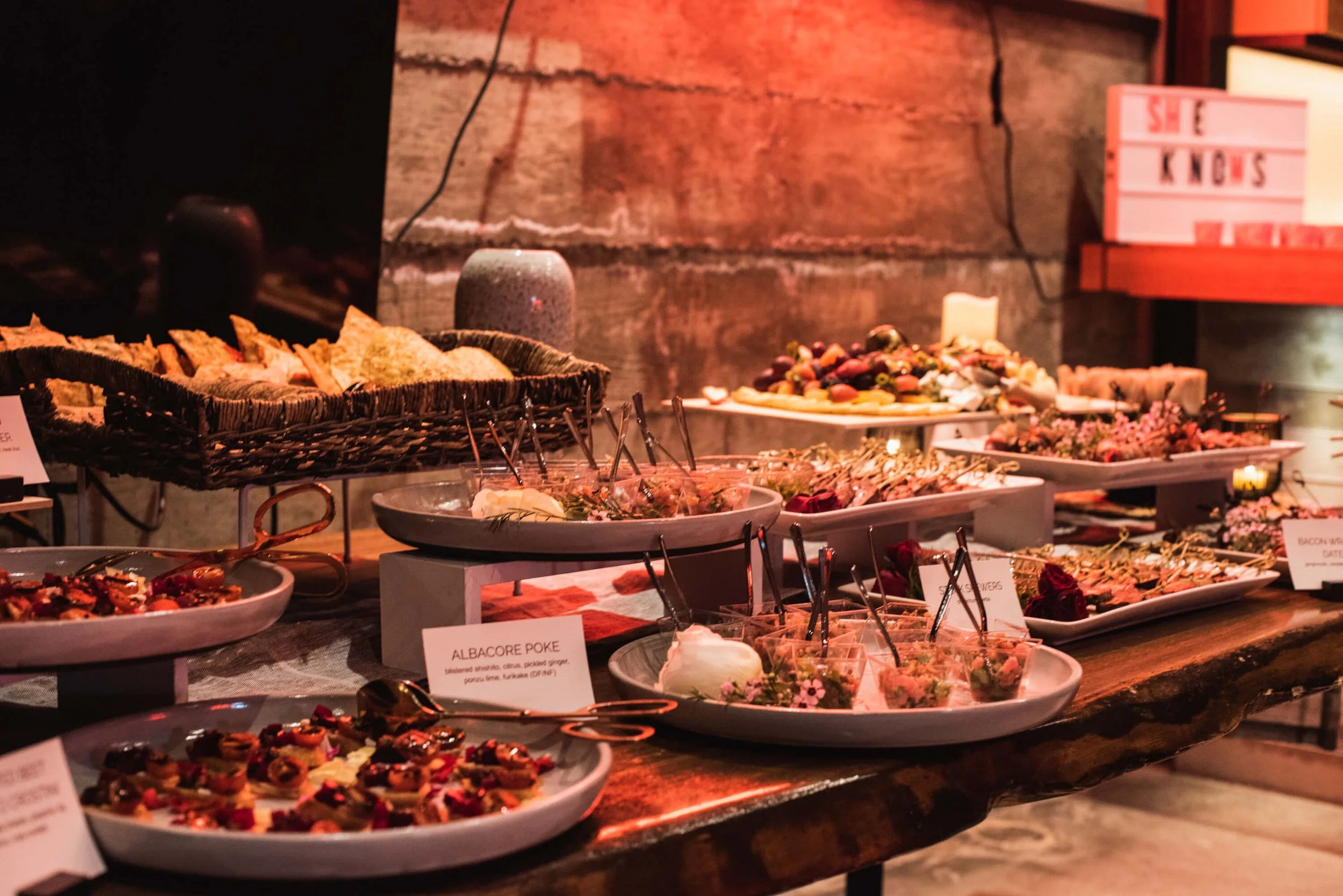 Platter of assorted appetizers and finger foods on a rustic wooden table, including crostini, salads, and skewers, in a warm ambient setting.