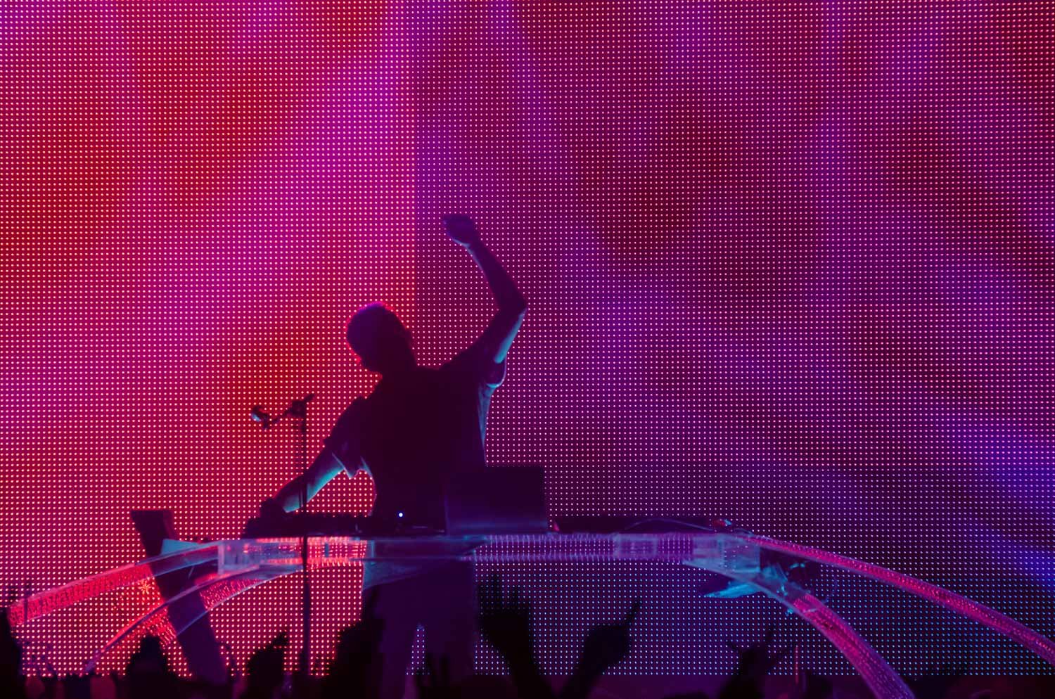 DJ performing on stage with colorful LED backdrop, silhouetted against pink and purple lights.