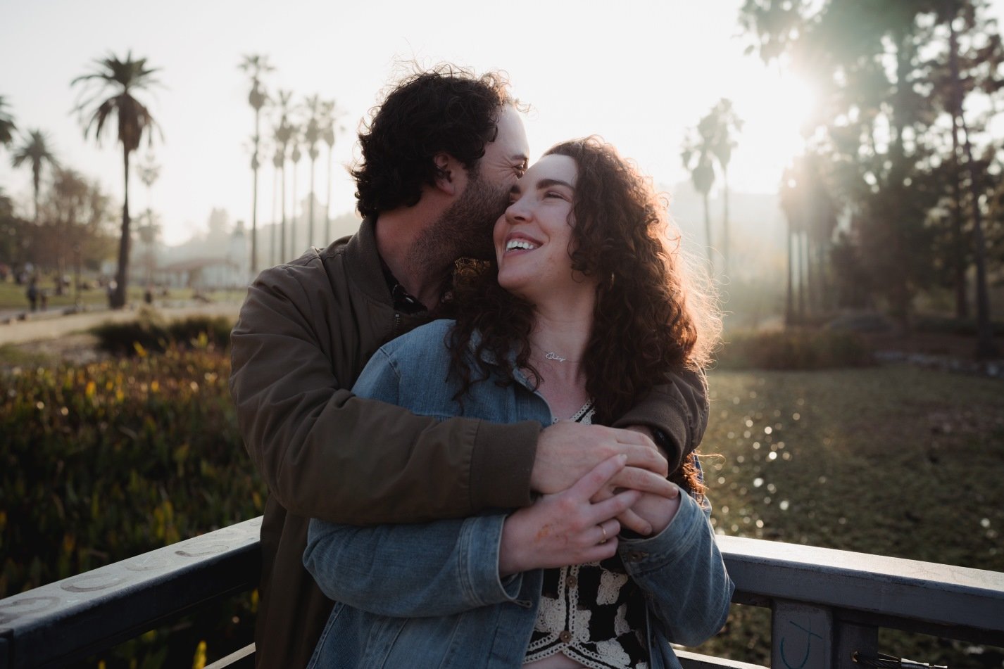 Happy couple hugging on a bridge with palm trees in the background at sunset.