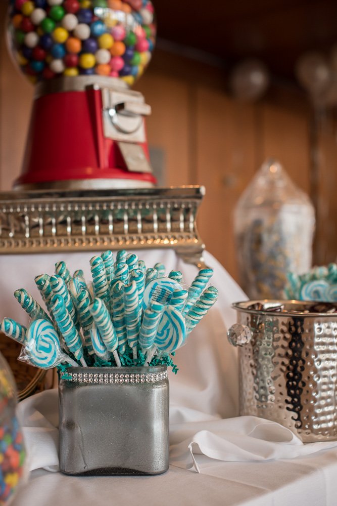 A jar filled with blue and white swirled peppermint candies in front of a gumball machine and other candy containers on a white tablecloth.