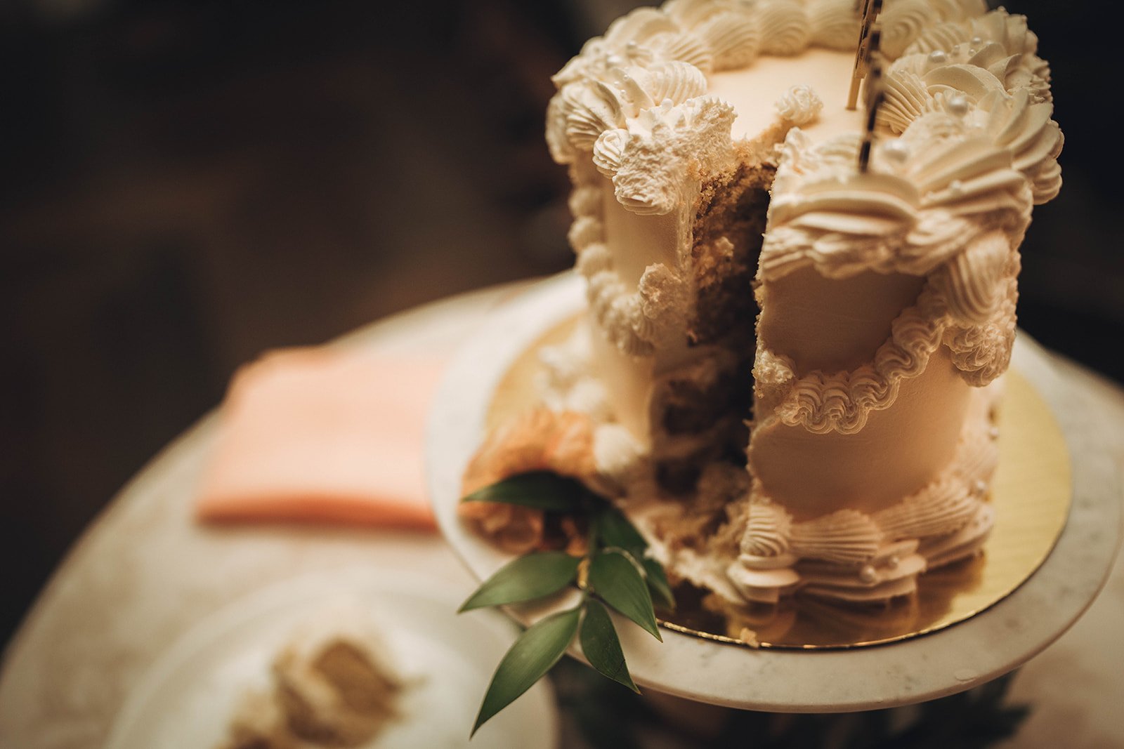 Close-up of a sliced cake with white frosting and decorative icing on a round table.