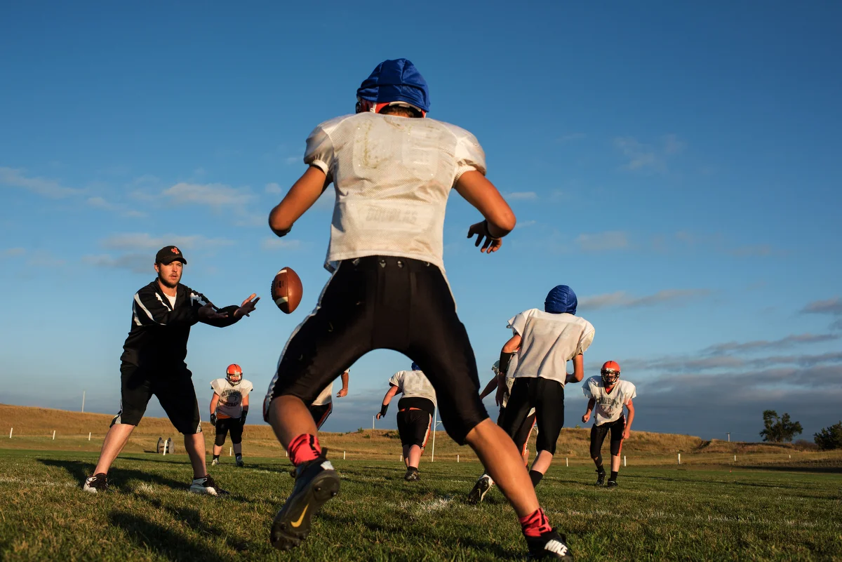 Coach Miller runs practice after school. Many of the players have to drive long distances home, and they generally work on the family ranch before school and finish their chores after practice.