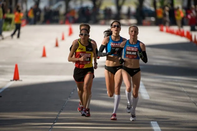 How did you do on yesterday’s photo of 3 foot strikes ? Now, look at the women ! Almost pristine ! Still a little evidence of cross over gait in each of them, but pretty darn good ! The feet are falling under the body mass, not good for sprinting, but utilized more in endurance athletes. If you have enough abdominal and hip frontal stabilzers (ie. G. Medius et al) you can play safely with the efficiency factor. If you do not have the strength, you sacrifice efficiency and risk injury at multiple sites in the lower limb. The more cross over you have, the more the foot will strike in inversion (more lateral foot strike), then you much hope you have enough gluteus medius strength at the hip, medial knee stability strength and ankle/arch strength in muscles like the tibialis posterior. Kara Goucher and Shalane Flanagan, right, shown here leading the 2012 Olympic Trials Marathon, Photo: Kurt Hoy/Competitor