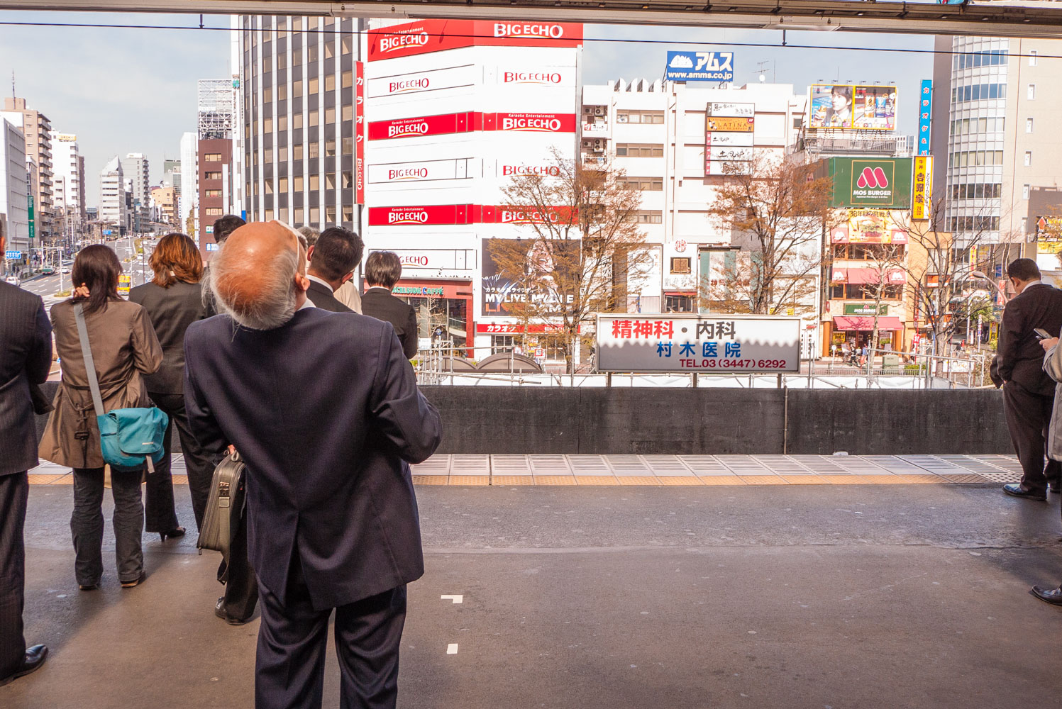  An office worker in gray suit exercises while waiting for a train at Gotanda Station, he arches his back leaning back and looks up high. 