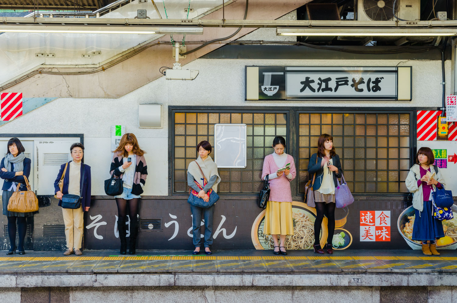  At Nippori Station seven women wait for a train, all are different ages, some are young, some are not,&nbsp;&nbsp;each doing something different, each in different style of dress 