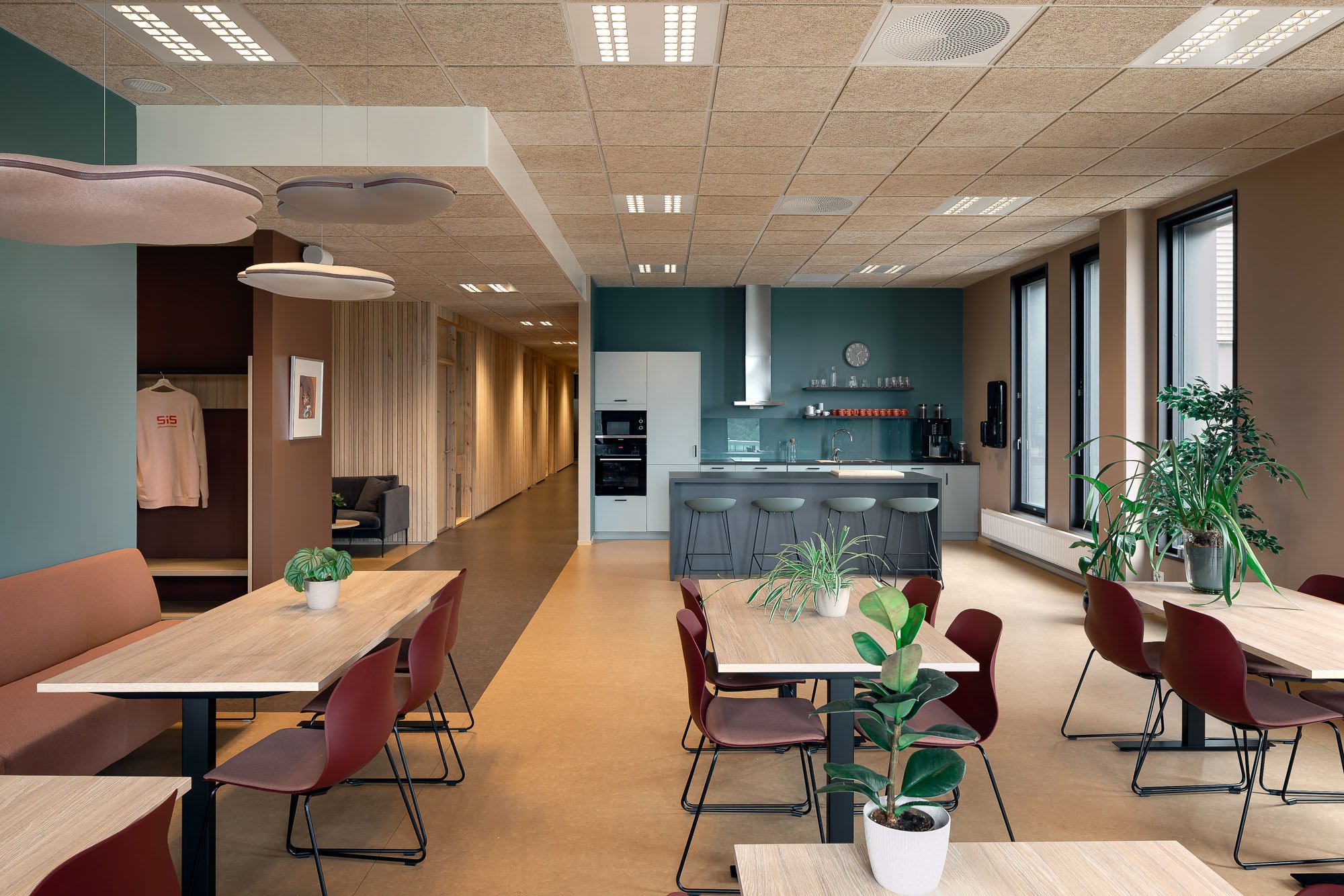 Moderne kjøkken og spisestue med tre bord og stoler, grønne planter, kjøkkenskap, store vinduer