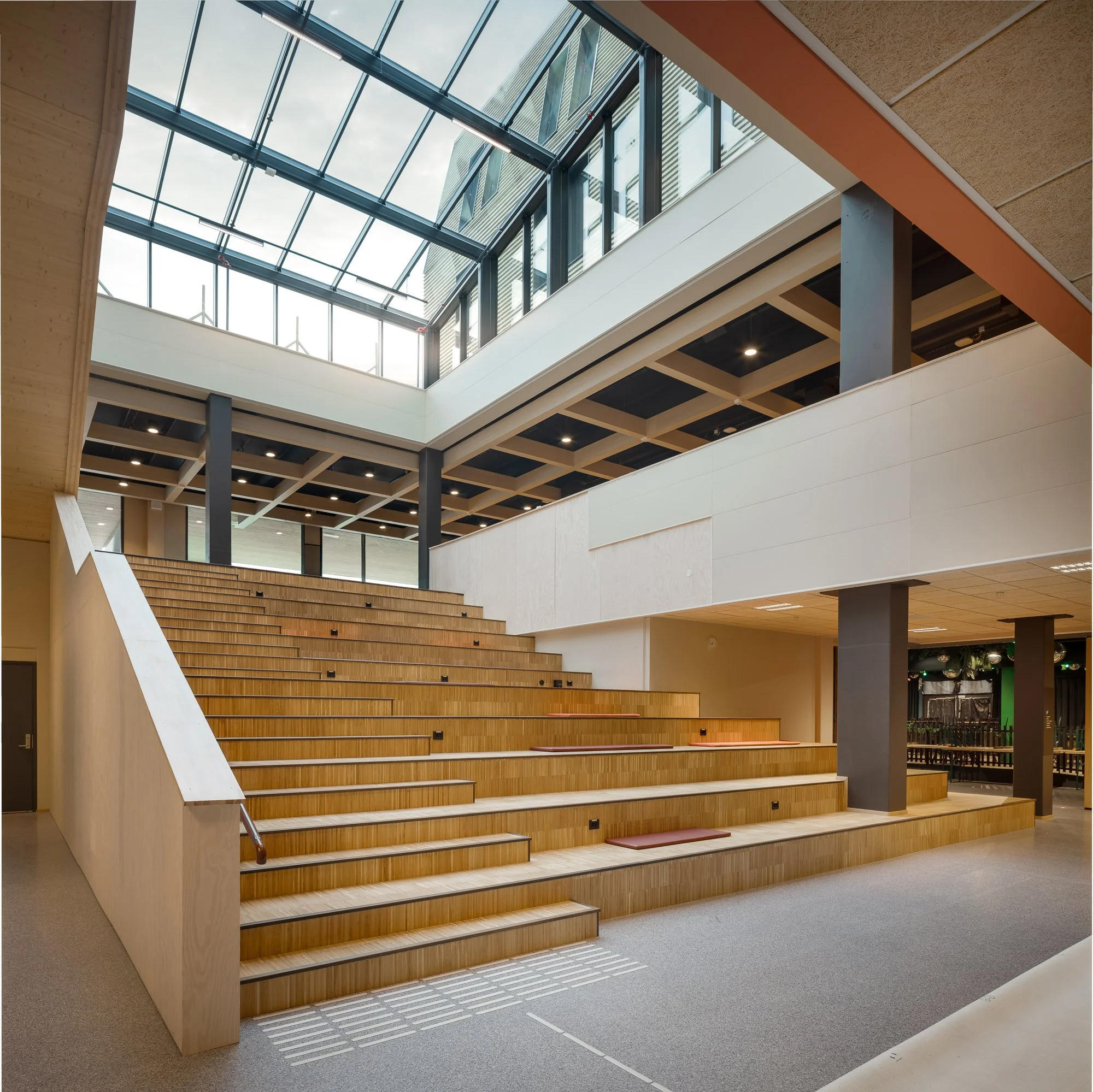 Innendørs trapp med tre-trinn og sitteplasser, tak med glasspanel som slipper inn naturlig lys.